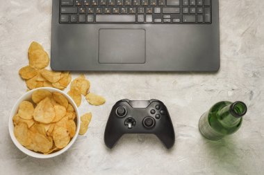 Dizüstü bilgisayar, Gamepad, patates cipsi, şişe bira hafif bir taş zemin üzerine. Bilgisayar oyunları ve eğlence kavramı.