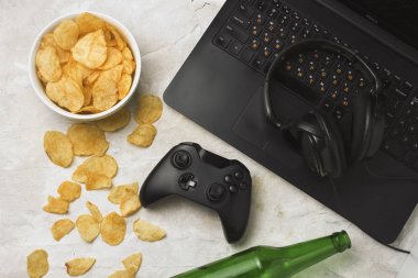 Dizüstü bilgisayar, Gamepad, kulaklık, patates cipsi, şişe bira hafif bir taş zemin üzerine. Bilgisayar oyunları ve eğlence kavramı.