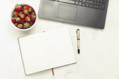 Dizüstü bilgisayar, günlük ve beyaz bir ışık taş zemin üzerine çilek plakalı. Evde rahat bir ortamda çalışma kavramı. Düz yatıyordu, en iyi görünümü.