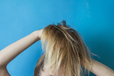 Kızın saçlarını ellerinin üzerinde mavi bir arka plan ile bir saç modeli oluşturmak için hazırlar. Modern tarz.