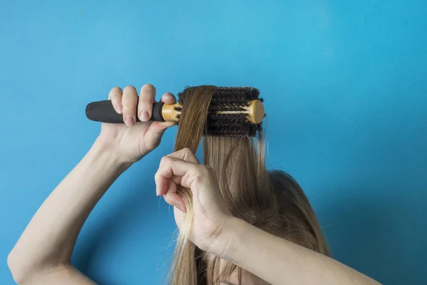 Girl combs her hair with a comb to create a hairstyle on a blue background. Modern style. Minimalism style.