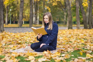 Genç hamile kız bir ekose bir sonbahar parkta oturan bir kitap okur. Başlangıcı sonbahar ve rekreasyon açık kavramı.