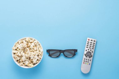 Patlamış mısırlı kase, Imax gözlükleri, mavi arka planda televizyon için uzaktan kumanda. Ev sineması kavramı, sinemanın yenilikleri, boş zaman. Düz yatış, üst görünüm.