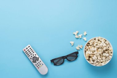 Patlamış mısırlı kase, Imax gözlükleri, mavi arka planda televizyon için uzaktan kumanda. Ev sineması kavramı, sinemanın yenilikleri, boş zaman. Düz yatış, üst görünüm.