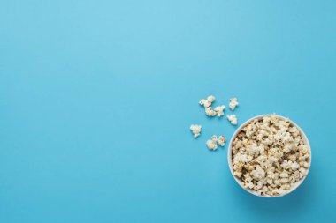 Mavi arka planda patlamış mısır kasesi. Ev sineması, sinema, boş zaman kavramı. Düz yatış, üst görünüm.
