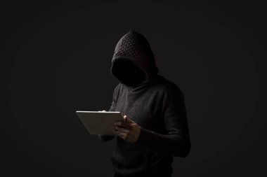 Kapüşonlu bir kukuleta ile yüzü olmayan adam bir tablet karanlık bir arka plan üzerinde onun elinde tutar. Kullanıcı veri kesmek kavramı. Kesmek kilit, kredi kartı, bulut, e-posta, şifre, kişisel dosyaları