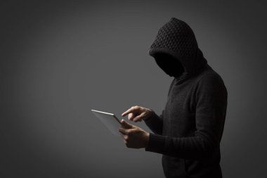 Kapüşonlu bir kukuleta ile yüzü olmayan adam bir tablet karanlık bir arka plan üzerinde onun elinde tutar. Kullanıcı veri kesmek kavramı. Kesmek kilit, kredi kartı, bulut, e-posta, şifre, kişisel dosyaları