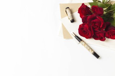 Buket kırmızı gül ve bir not, beyaz bir arka plan üzerinde bir dolma kalem bir zarf. Kavramı bir romantik hediye. Düğün Temalar.