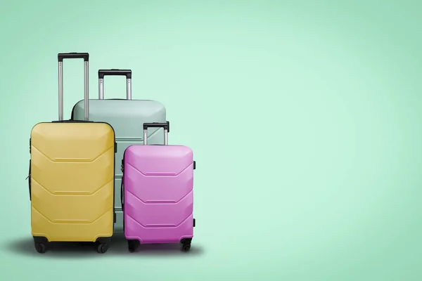 三个多色塑料手提箱在车轮上的绿色背景 旅行概念 假期旅行 — 图库照片