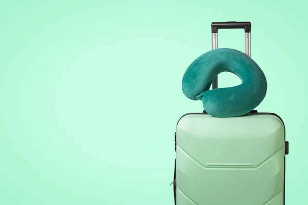 Plastic suitcase and travel pillow on a green background. Concept of travel, business trips, trips to visit friends and relatives.