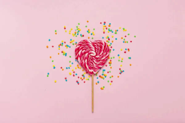 Heart Lollipop and multi coloured sweets on a gently pink background. Concept of sweets and candies. Sweet gift. Sweet love. Flat lay, top view.