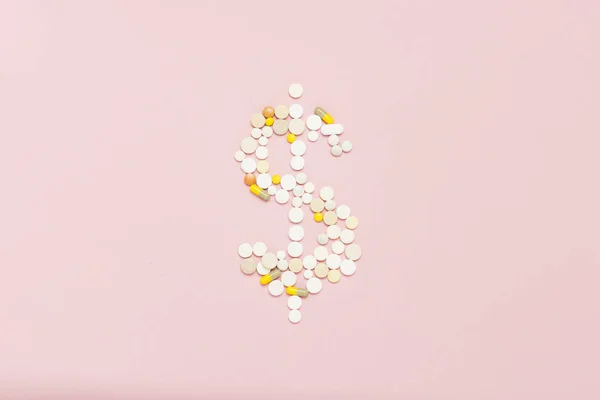 Pills laid out in the form of a dollar on a light pink background. Concept of high prices for drugs, expensive medicine, vitamins and minerals for women. Breast cancer, menopause. Flat lay, top view.