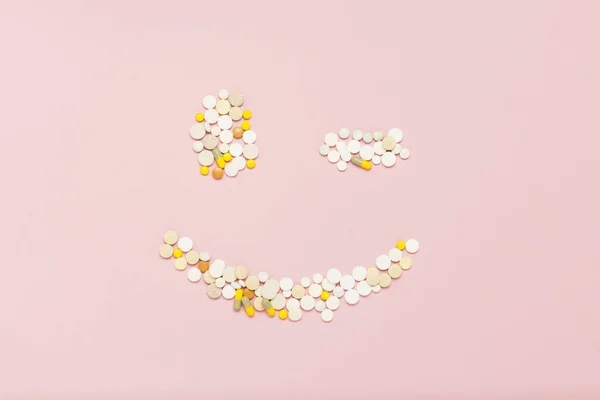 Pills laid out in the sign winking face on a light pink background. Concept vitamins and minerals for women, pregnancy, women's health care. Flat lay, top view.