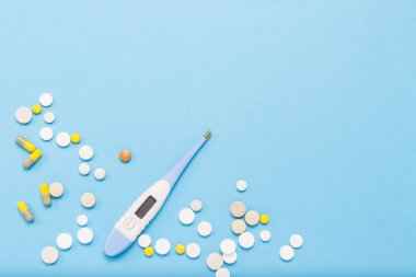 Elektronik termometre ve çevresinde haplarla mavi bir arka plan. Düz yatıyordu, en iyi görünümü.