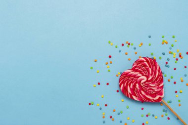 Bir kalp ve mavi bir arka plan üzerinde renkli tatlılar şeklinde pembe lolipop. Şekerleme, aşk, sevilen bir için bir hediye kavramı. Düz yatıyordu, en iyi görünüm, kopya alanı.
