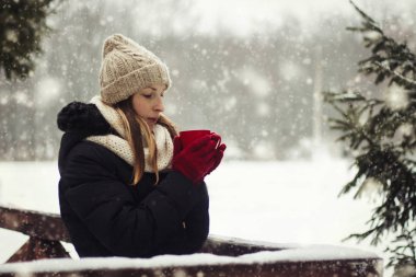 Genç kız kırmızı eldiven sıcak çay kış manzara arka plan üzerinde kırmızı fincanla kar yağışı sırasında tutar..