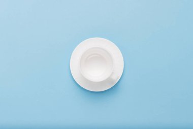 Boş beyaz fincan tabağı üzerinde mavi bir arka plan ile. Düz yatıyordu, en iyi görünümü.
