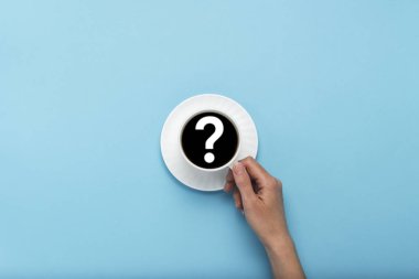 Mavi bir arka plan üzerinde siyah kahve beyaz bir bardak tutan el. Soru işareti. Düz yatıyordu, en iyi görünümü.