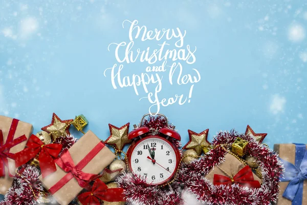 Red alarm clock, Christmas decorations, gifts on a blue background with snow. Added text Merry Christmas and happy new year. Flat lay, top view.