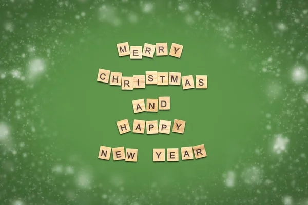 Text of Happy Christmas and Happy New Year laid out of wooden plates with letters on a green background with snow. Minimalism. Flat lay, top view.