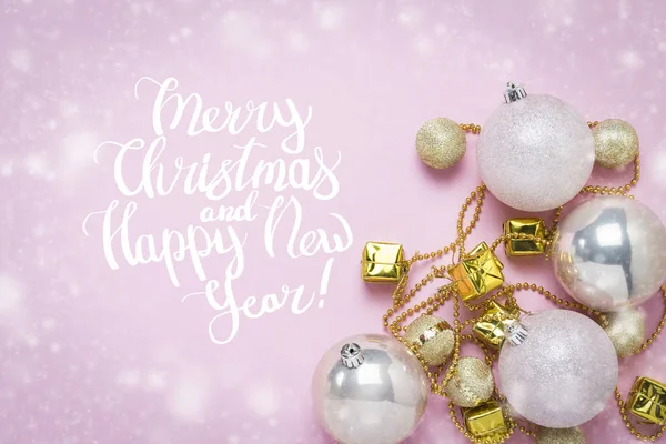 Christmas-tree decorations, balls, garland on a light pink background with snow. Added text Merry Christmas and Happy New Year. Flat lay, top view.
