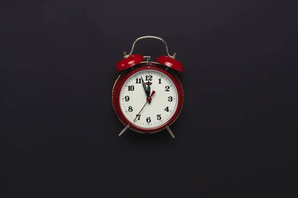 Red retro alarm clock on black background. Minimalism. Flat lay, top view.