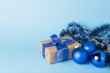 Hediye kutusu ile mavi kurdele, mavi bir arka plan üzerinde Noel süsleri. Minimalizm. Sevdiklerinize hediye kavramı.