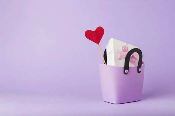 Small plastic bag for shopping, gift boxes, heart on a stick, purple background. Concept of pre-holiday shopping, gifts for friends and relatives, Christmas sale, Black Friday, Cyber Monday.