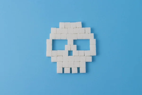 Skull of cubes of sugar and pieces of sugar on a blue background. Concept Sugar kills and harm sweet on the human body