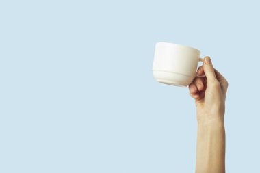 Sıcak kahve veya çay ışık mavi zemin üzerine beyaz bir bardak tutan el. Sıcak kahve veya çay ile kahvaltı konsepti.