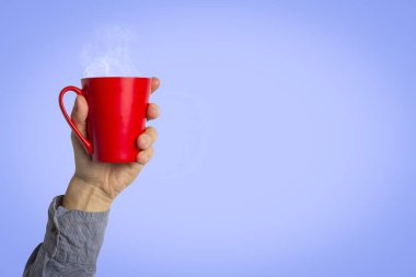 Male hand holding a red cup with hot coffee or tea on a light blue background. Breakfast concept with hot coffee or tea. clipart