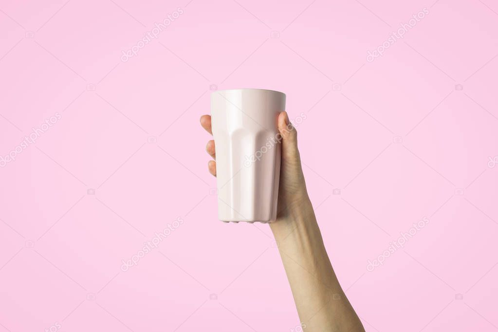 Female hand holding a purple cup with hot coffee or tea on a light pink background. Breakfast concept with hot coffee or tea.