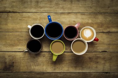 Bir sürü kahve ve kahve içecekler ahşap arka plan üzerinde renkli bardak. Kavram kahvaltı kahve, kahve arkadaş grubu. Düz yatıyordu, en iyi görünümü.