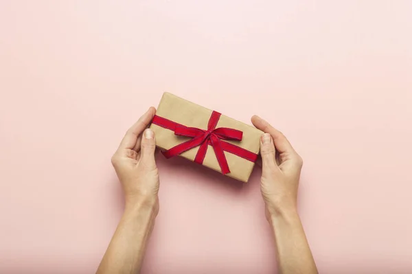 女性手拿着一个礼品盒在粉红色的背景与问号 惊喜的概念 等待节日 圣诞节 婚礼的礼物 平面布局 顶部视图 — 图库照片