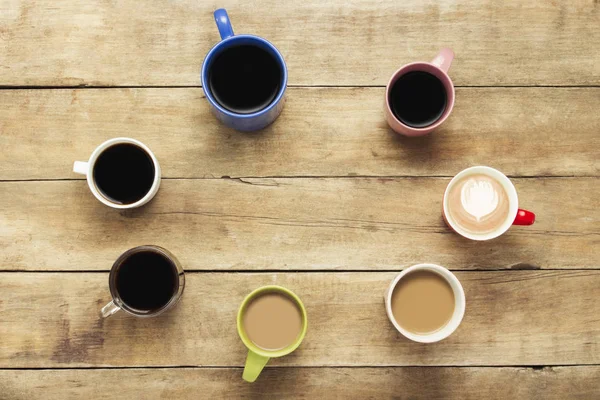 A lot of multicolored cups with coffee and coffee drinks on a wooden background. Ellipse form. Concept breakfast with coffee, coffee with friends. Flat lay, top view.