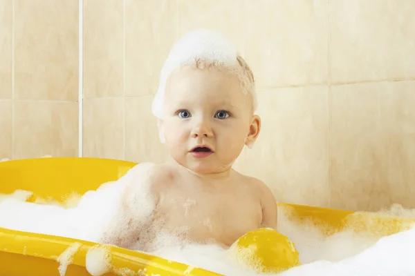 Little baby takes a bath in a yellow bath with bubbles and foam. The concept of happy child, love for bathing