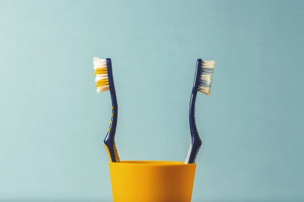 Duas Escovas Dentes Uma Xícara Plástica Afastam Outro Contexto Azul — Fotografia de Stock