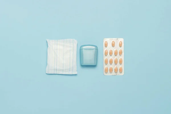 Feminine hygiene tampons, box for shipping and storage and sanitary pad, pain pills on a blue background. Concept of feminine hygiene during menstruation, menstruation kit. Flat lay, top view