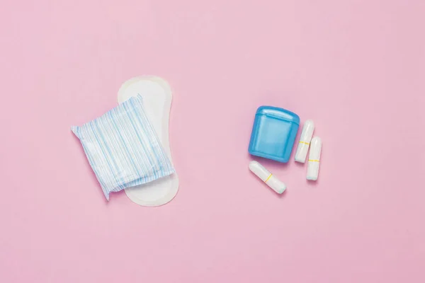 Feminine hygiene tampons, box for shipping and storage and sanitary pad on a pink background. Concept of feminine hygiene during menstruation, choice between pads and tampons. Flat lay, top view