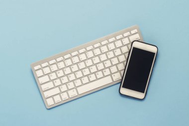 Mavi bir arka plan üzerinde klavye ve beyaz cep telefonu. İş kavramı, ofis işleri, mobil app ve Web sitesi. Düz yatıyordu, en iyi görünümü