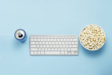 İçkili klavye ve teneke kutu, enerji içeceği, mavi arka planda bir kase patlamış mısır. Film izleme konsepti, TV programları, online spor etkinlikleri. Düz yatış, üst görünüm