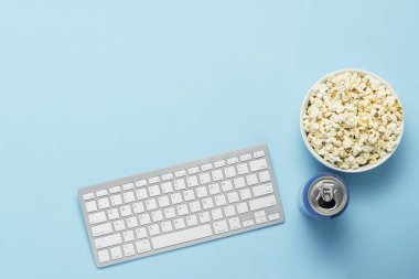 İçkili klavye ve teneke kutu, enerji içeceği, mavi arka planda bir kase patlamış mısır. Film izleme konsepti, TV programları, online spor etkinlikleri. Düz yatış, üst görünüm