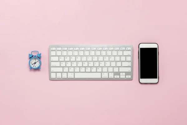 Keyboard, mobile phone and alarm clock on a pink background. Business concept. Flat lay, top view