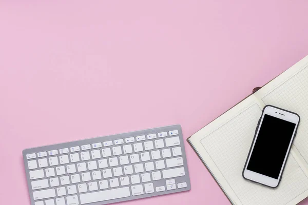 Keyboard, mobile phone and daily log on a pink background. Business concept. Flat lay, top view