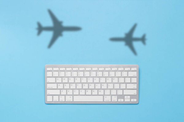 Keyboard and shadow of a flying plane on a blue background. The concept of buying tickets on the Internet online, booking tickets. Flat lay, top view