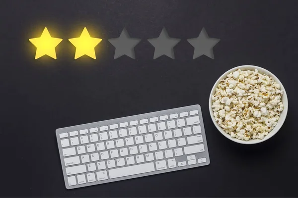Bowl of popcorn, keyboard on a black background. Added two stars rating. Reputation. Concept of watching movies, TV shows, sports. Audit and evaluation. Flat lay, top view