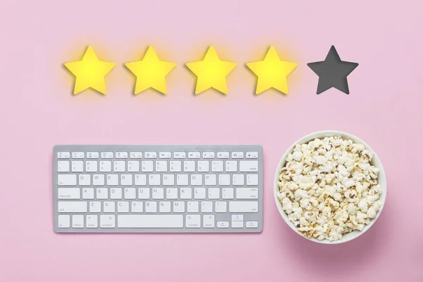 Bowl of popcorn, keyboard on a pink background. Added four stars rating. Reputation. Concept of watching movies, TV shows, sports. Audit and evaluation. Flat lay, top view
