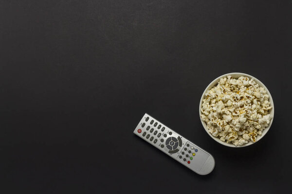 Чаша с попкорном и пультом от телевизора на черном фоне. Понятие просмотра телевизора, фильма, сериала, спорта, шоу. Плоский, вид сверху
