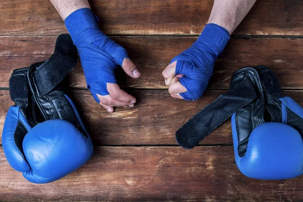 Men\'s hands in boxing bandages and boxing gloves on a wooden background. Concept preparation for boxing training or combat. Flat lay, top view.