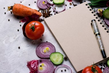 Defter, kalem, kesme tahtası ve açık renkli sebze. Yemek, vejetaryenlik ve sağlıklı beslenme kavramı.